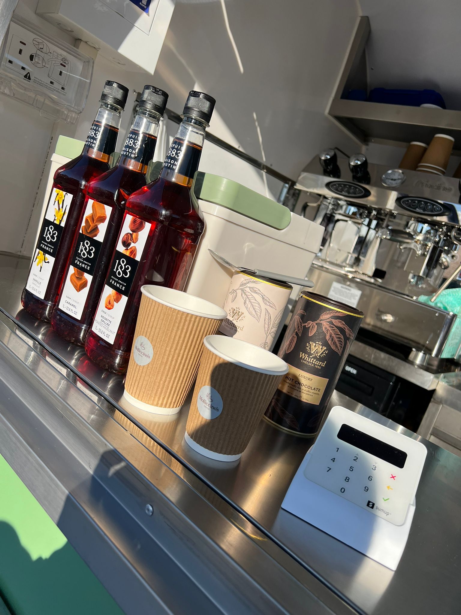 1883 flavour syrups, Molliccino's cups and card reader lined up on the trailer counter