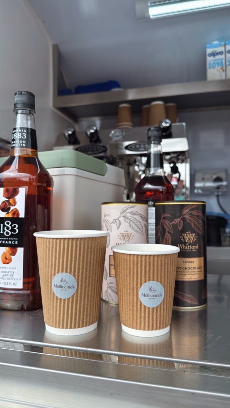 Molliccino's branded cups next to 1883 hazelnut syrup and Whittard luxury hot chocolate