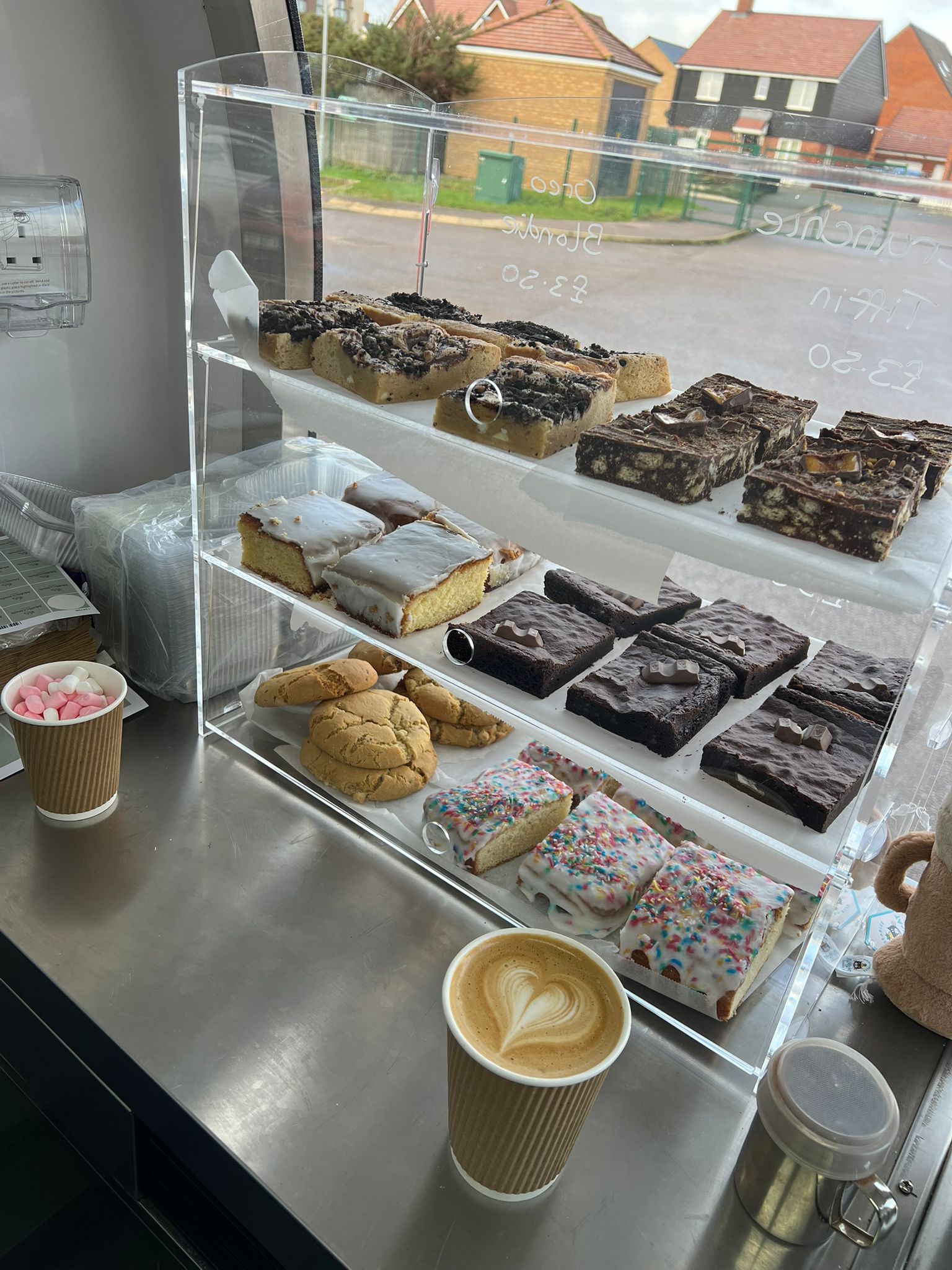 Food display cabinet filled with brownies, traybakes, cookies and pastries alongside a latte